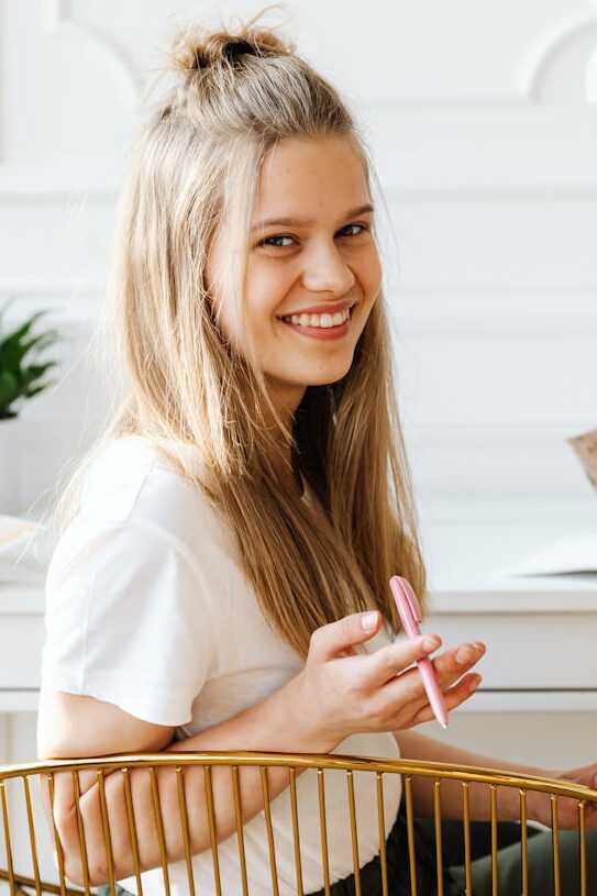 smiling girl sitting on a chair while holding a ball pen
